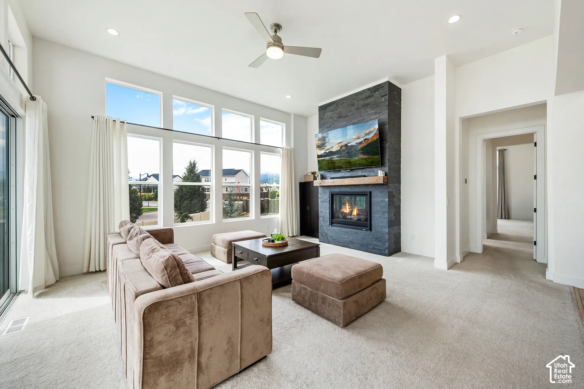 Living area featuring a stone-clad fireplace with wood mantle, high ceilings, recessed lighting, and large windows