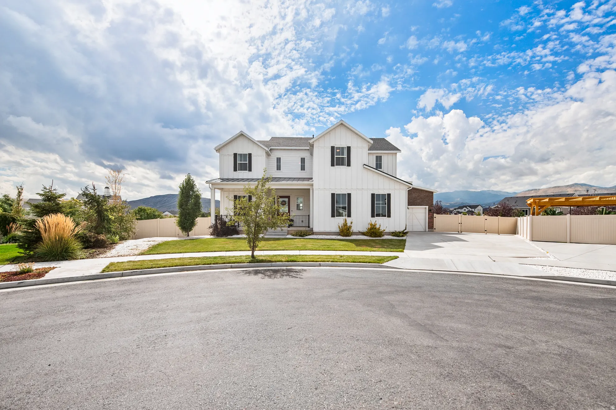 White board and batten exterior with dark shutters, covered front porch, attached garage, concrete driveway, and a pergola