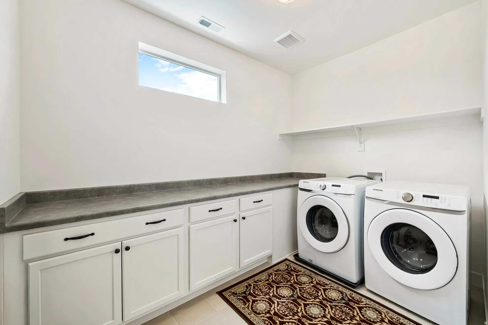 White cabinetry with dark hardware, gray countertop, and an elevated shelf