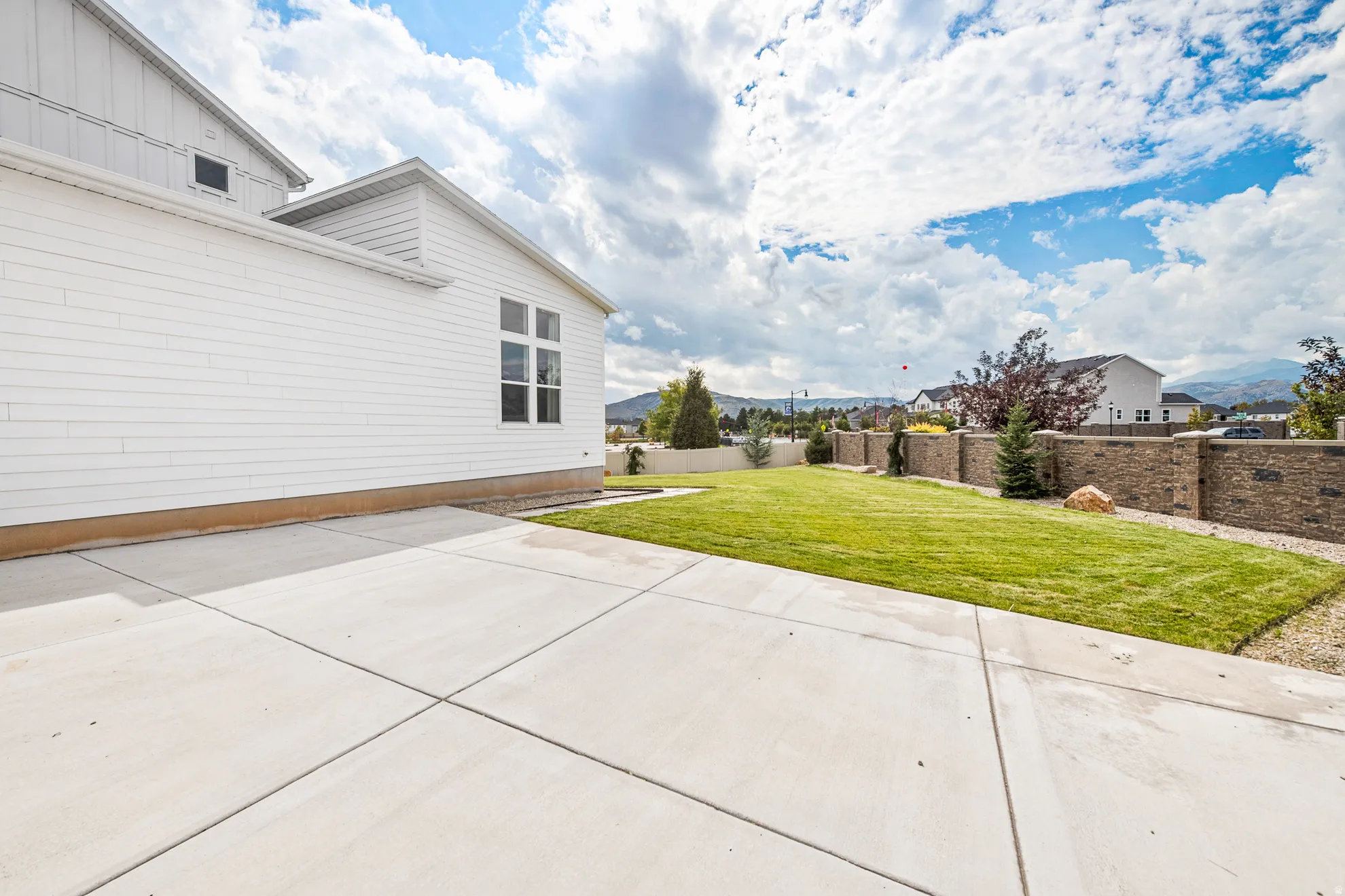 Expansive concrete patio, manicured lawn, and stone retaining wall