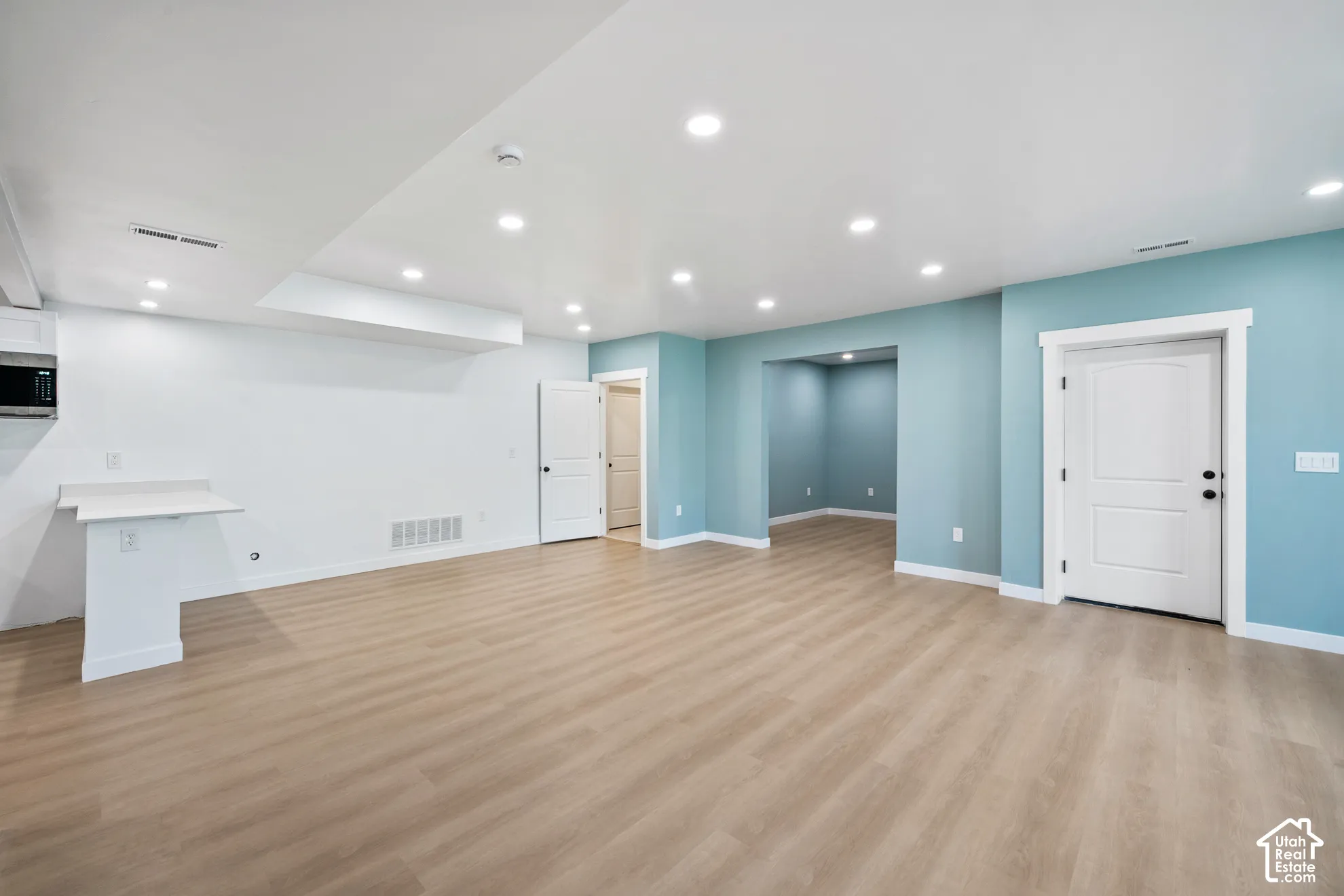 Recessed lighting, light wood-finish flooring, built-in microwave, white trim, and a built-in counter