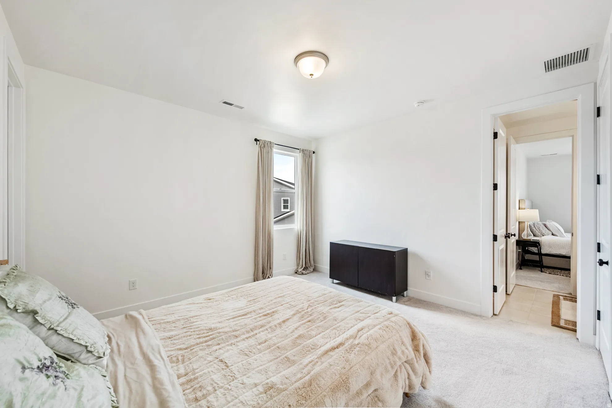 White walls with coordinating trim, neutral carpeting, and a single window with drapes
