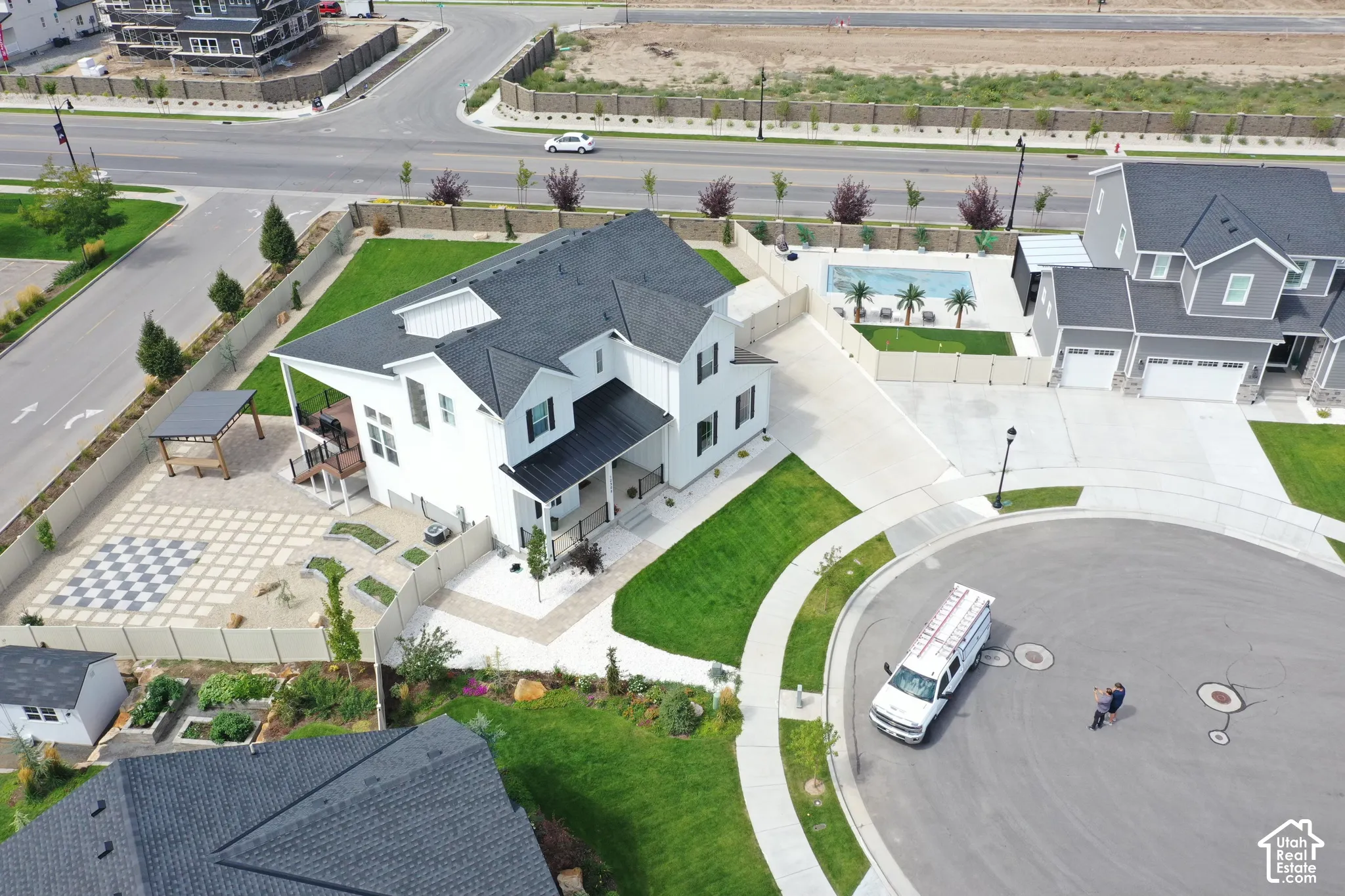 White exterior residence featuring a dark roof, covered porch, and rear patio with a checkerboard paver design