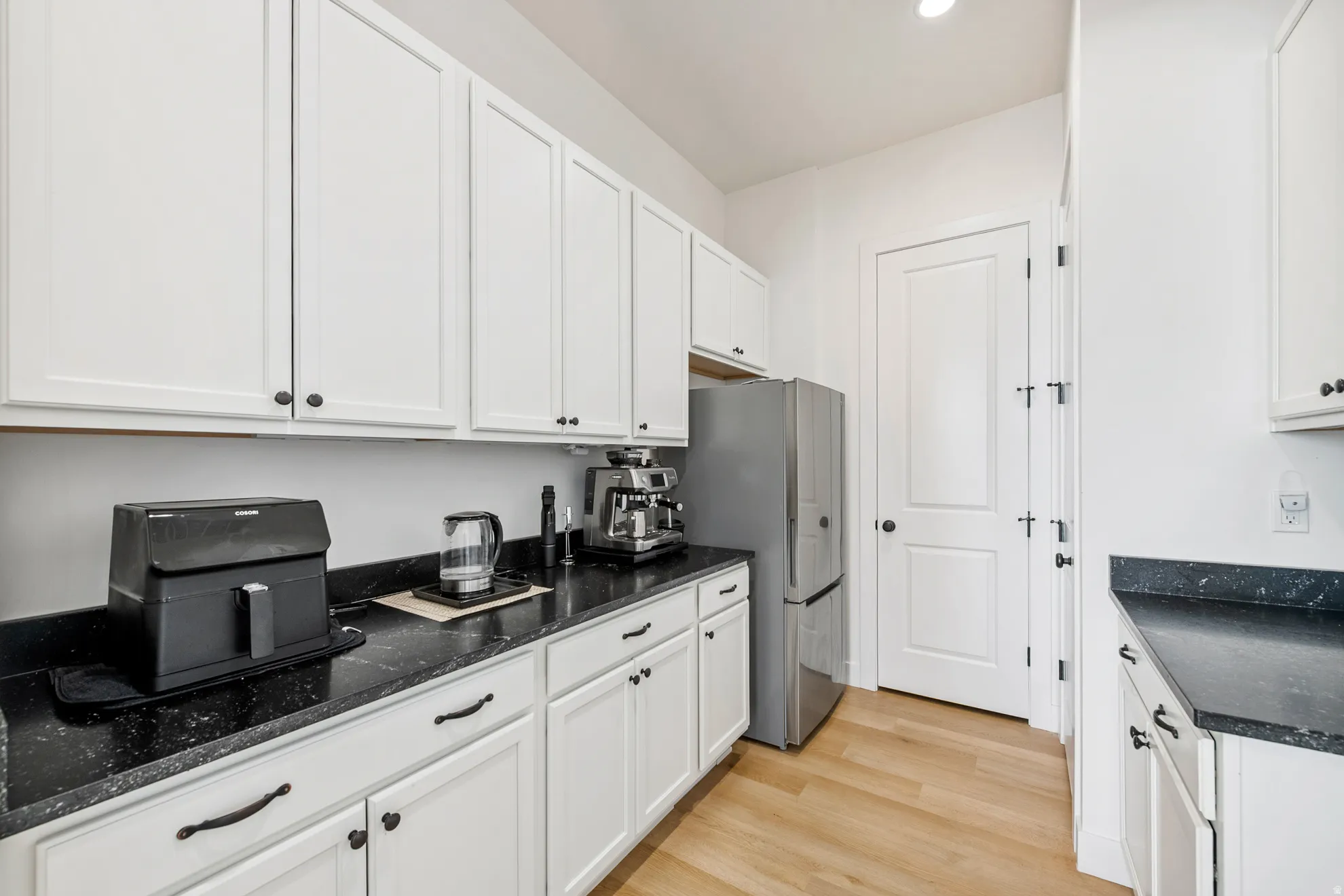White shaker-style cabinetry, dark speckled countertops, stainless steel refrigerator, white paneled doors, and wood-finish flooring