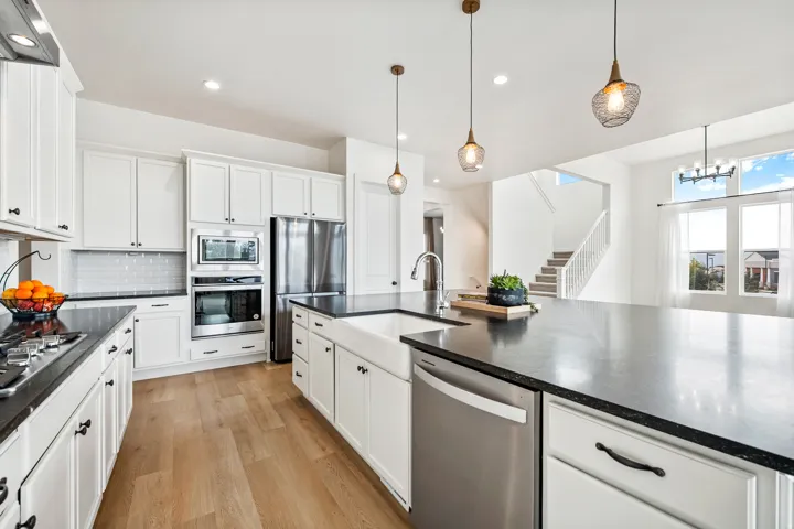 Gourmet kitchen featuring white cabinetry, dark countertops, wood-finish flooring, stainless steel appliances, and a farmhouse sink