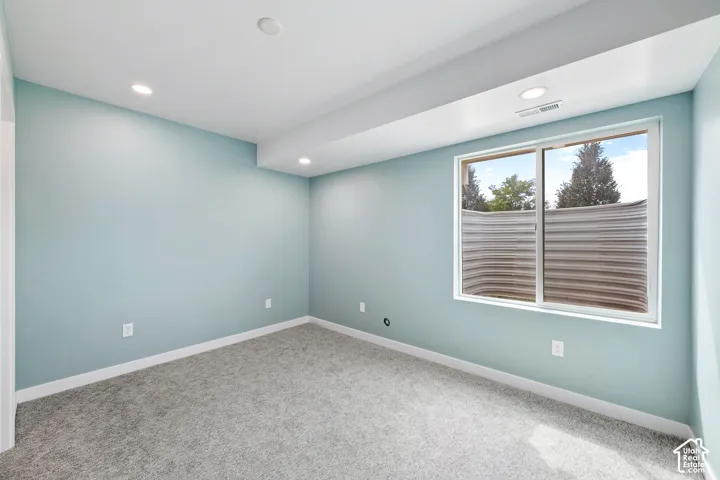 Recessed lighting, light-colored walls, window with metal window well, light gray carpet, white trim