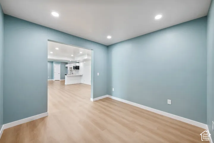 Recessed lighting, light wood-finish flooring, and a wide entryway to the kitchen featuring white cabinetry and appliances