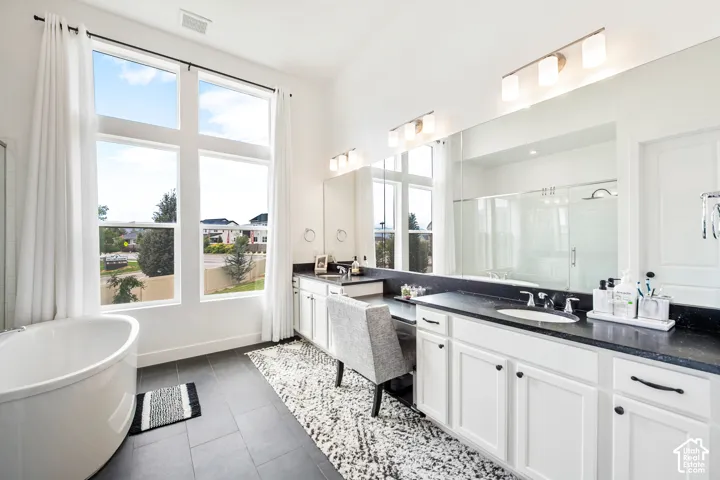 Freestanding oval soaking tub, expansive full-height windows, dual vanity with dark countertops, built-in makeup vanity, and a large mirrored wall