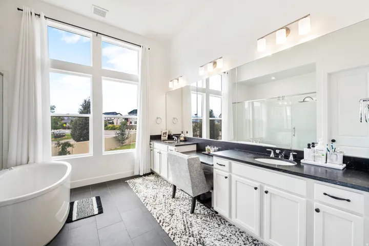 Freestanding oval soaking tub, expansive full-height windows, dual vanity with dark countertops, built-in makeup vanity, and a large mirrored wall