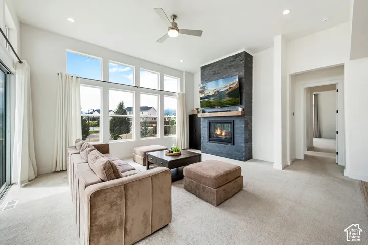 Living area featuring a stone-clad fireplace with wood mantle, high ceilings, recessed lighting, and large windows