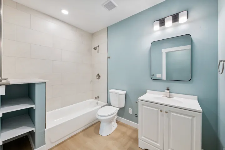 White subway tile shower surround with a built-in tub, wood-finish flooring, white vanity with integrated sink, and a modern rectangular mirror