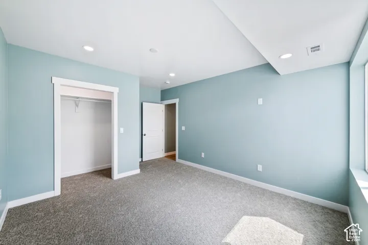 Recessed lighting, plush carpeting, light-toned walls, and an integrated closet with shelving