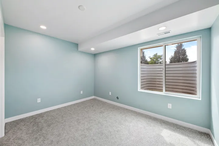 Recessed lighting, light-colored walls, window with metal window well, light gray carpet, white trim