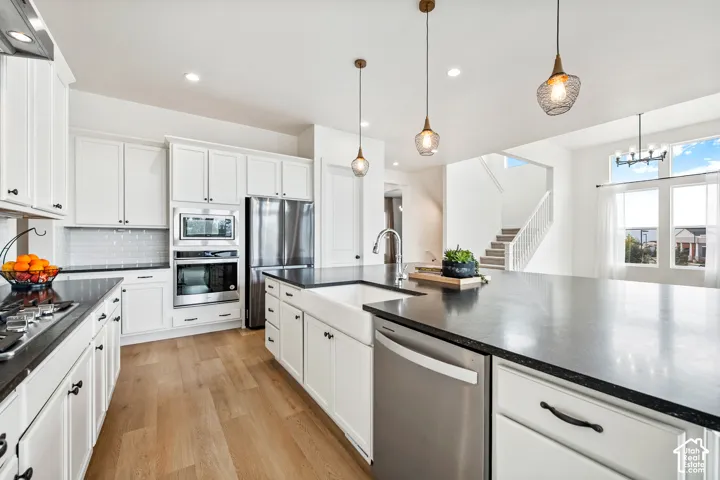 Gourmet kitchen featuring white cabinetry, dark countertops, wood-finish flooring, stainless steel appliances, and a farmhouse sink