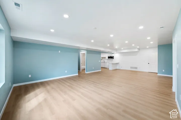 Spacious open-concept room featuring light wood-finish flooring, recessed lighting, and a partial kitchen with white cabinetry