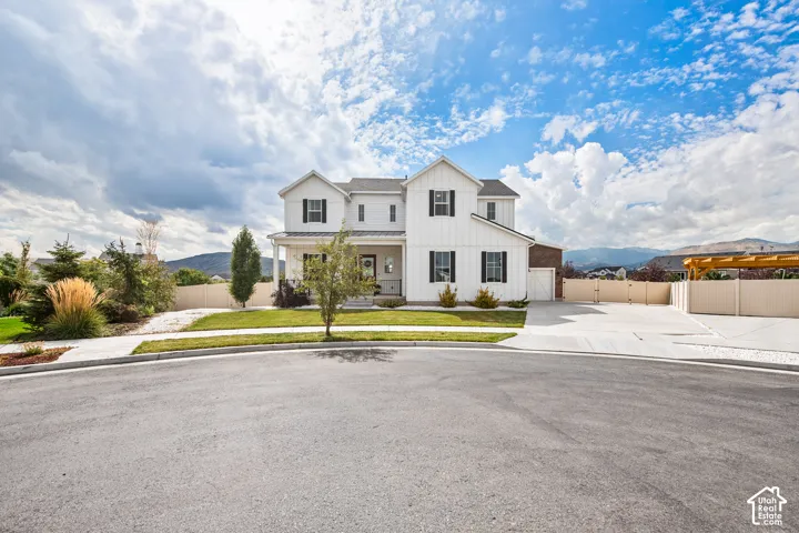 White board and batten exterior with dark shutters, covered front porch, attached garage, concrete driveway, and a pergola