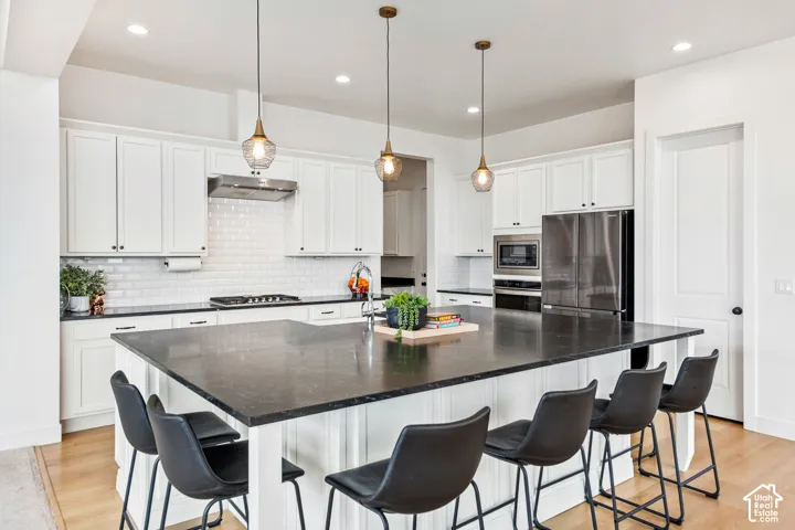 Kitchen featuring a large island with dark countertop, white shaker cabinetry, stainless steel appliances, and wood-finish flooring