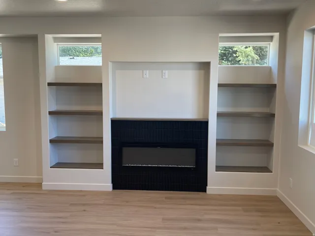 Built-in electric fireplace with black surround, recessed television niche, built-in shelving with wood-finish shelves, and wood-finish flooring