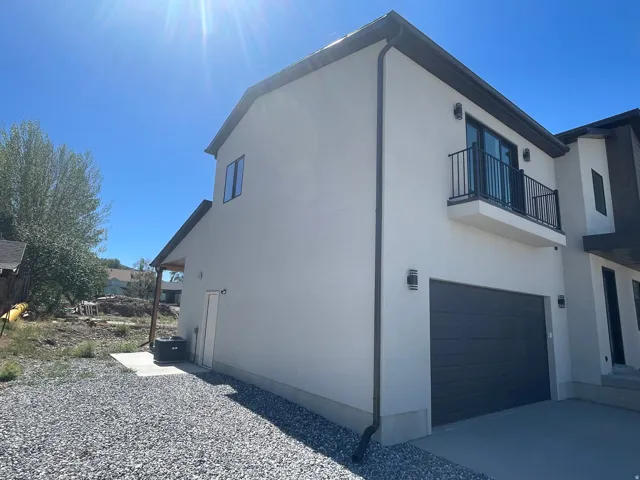 Modern/contemporary exterior with a smooth stucco finish, dark trim, and a second-story balcony featuring a black metal railing.