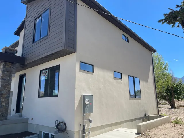 Stucco exterior with dark-framed windows, stone accent column, and modern horizontal siding detail
