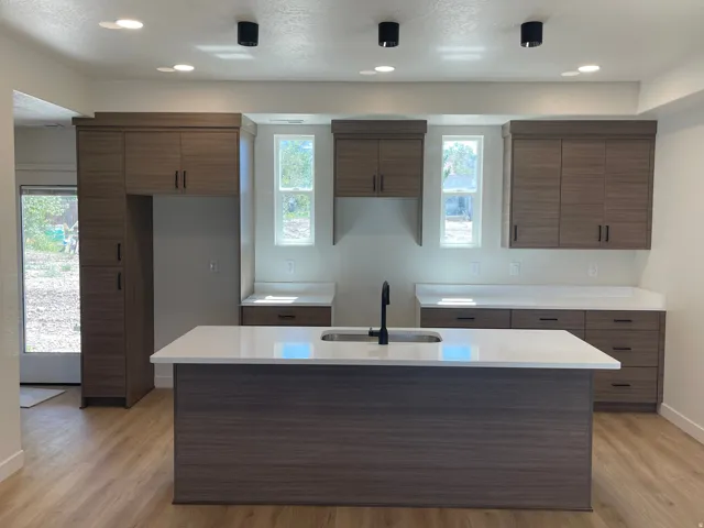 Wood-finish flooring throughout the kitchen, featuring a central island with an integrated sink and matte black faucet