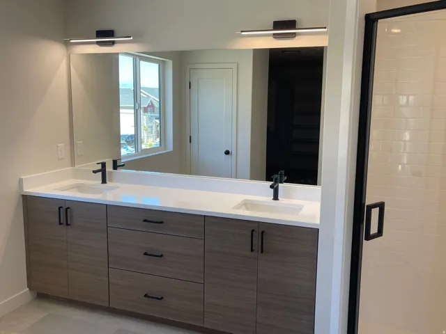 Master bathroom dual vanity with wood-finish cabinetry, white countertops, matte black fixtures, and an oversized mirror