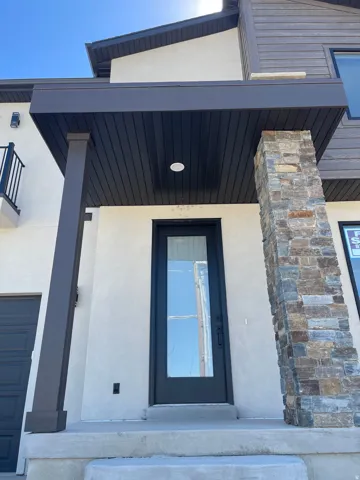 Entryway with a glass-paneled door, stone-clad pillar, and an overhead lighting.