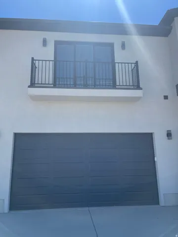 Second-story balcony with metal railing, sliding glass doors, and exterior lighting.