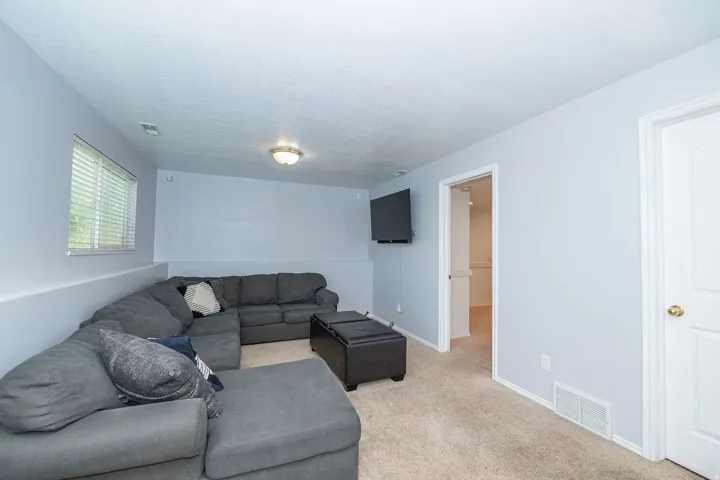 Basement living room with light-colored carpeted flooring with light blue walls, white trim, and a window with blinds.