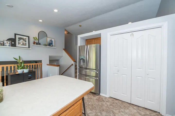 Kitchen island with a laminate countertop, stainless steel refrigerator, white bi-fold pantry doors, and recessed lighting.