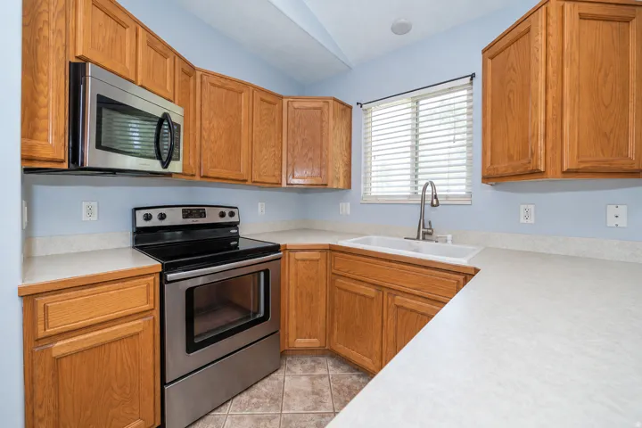Full kitchen with wood cabinetry, stainless steel appliances, light countertops, and tile flooring.