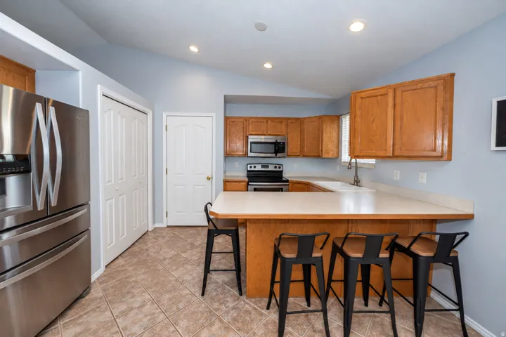Kitchen featuring tile flooring, vaulted ceiling, wood cabinetry, built-in stainless steel appliances, and a breakfast bar with solid surface countertops.