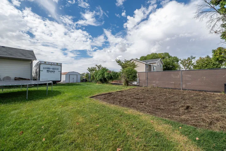 Expansive backyard featuring a manicured lawn, a cultivated garden area, and a privacy-screened chain-link fence