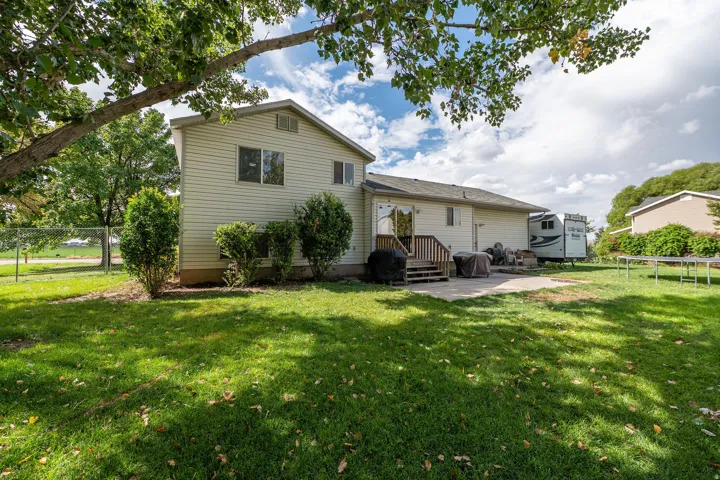 Expansive green lawn with mature trees, stone patio, and wood-finished deck