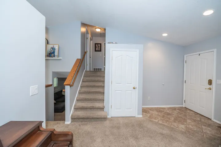 Carpeted staircase with wood-finish handrail & coat closet.
