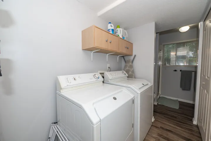 Integrated laundry area with wood-finish flooring, overhead cabinetry, and a full-size washer and dryer