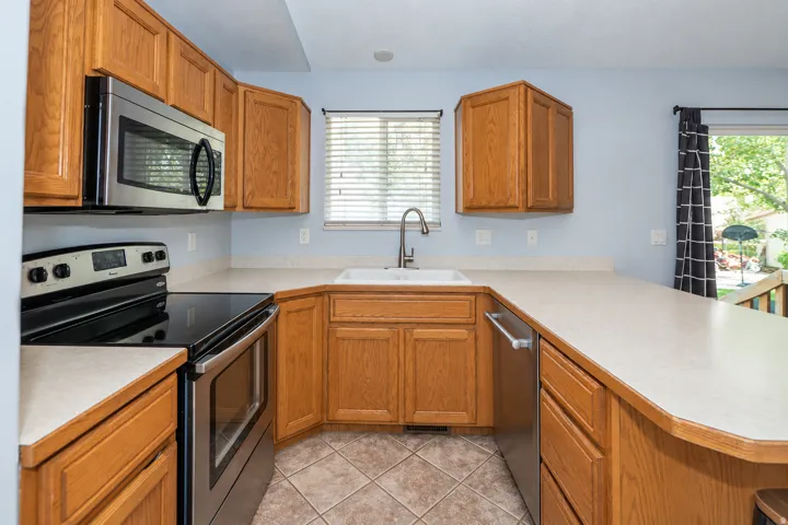 Kitchen featuring wood cabinetry, stainless steel appliances, a corner sink, and tiled flooring.