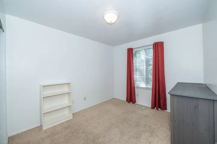 Neutral wall color with a window featuring horizontal blinds, carpeted flooring, and a ceiling-mounted light fixture