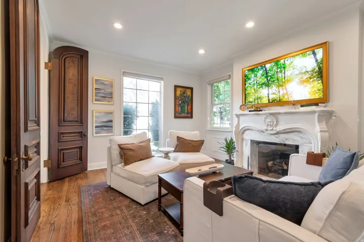 Hardwood flooring, ornate carved wood door, detailed fireplace mantel with a marble surround, recessed ceiling lighting, and multiple windows