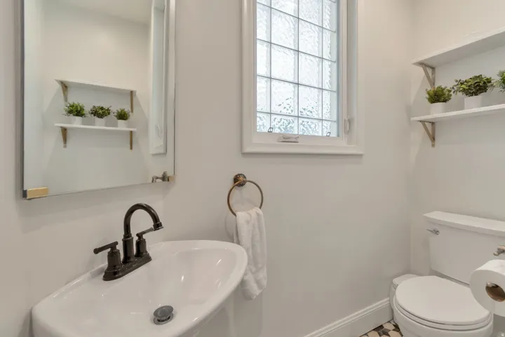 Wall-mounted vanity sink with a dark bronze faucet, framed mirror, and a privacy window