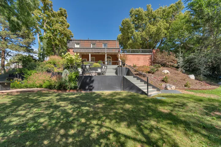 Expansive grass lawn, multi-level hardscaping, mature trees, brick exterior, and a built-in outdoor staircase