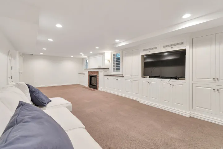 Recessed lighting, extensive built-in cabinetry, integrated media center, tiled fireplace surround, and plush carpet flooring