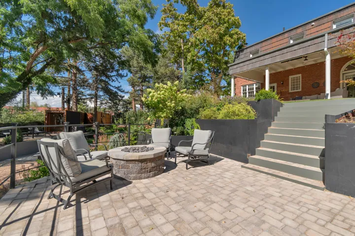 Paver patio with a stone-clad fire pit, tiered landscaping, and a multi-level brick exterior