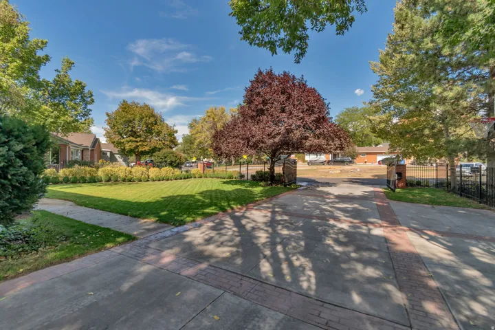 Expansive front lawn with manicured landscaping, mature trees, and a concrete driveway with brick accents
