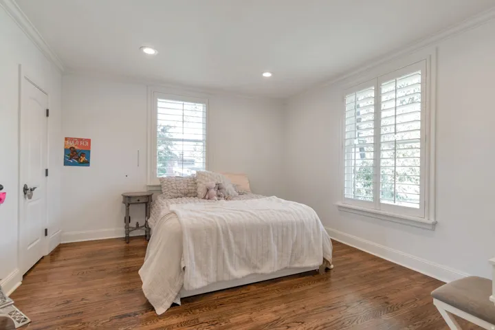 Hardwood flooring, two windows with white plantation shutters, recessed lighting, and crown molding