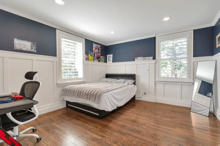 Hardwood flooring, recessed lighting, white board and batten wall paneling, crown molding, and two windows with plantation shutters