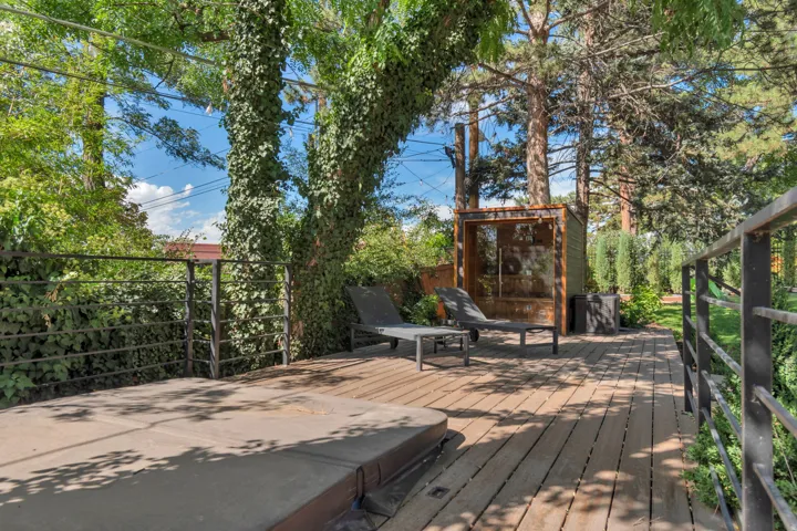 Expansive wood deck with a hot tub, surrounded by mature trees and lush greenery