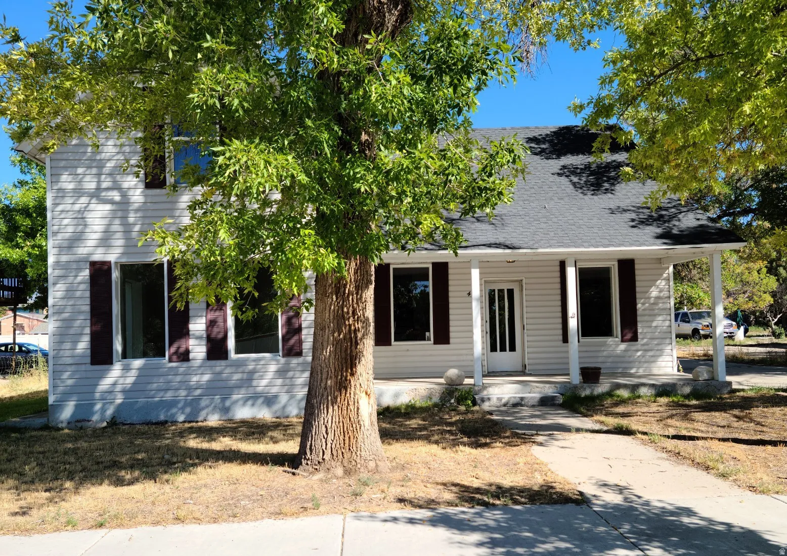 Two-story exterior with white siding, dark shutters, covered front porch, and mature trees