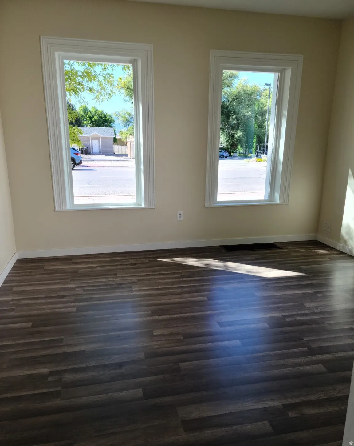 Wood-finish flooring with light-toned walls and two windows featuring white trim