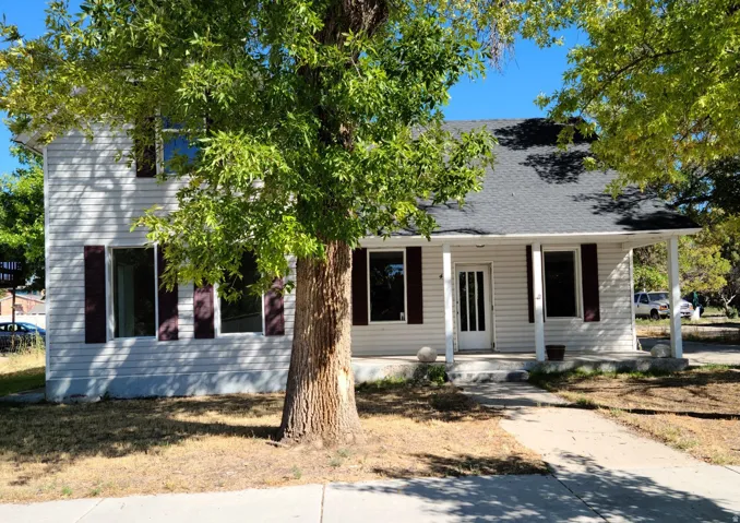 Two-story exterior with white siding, dark shutters, covered front porch, and mature trees